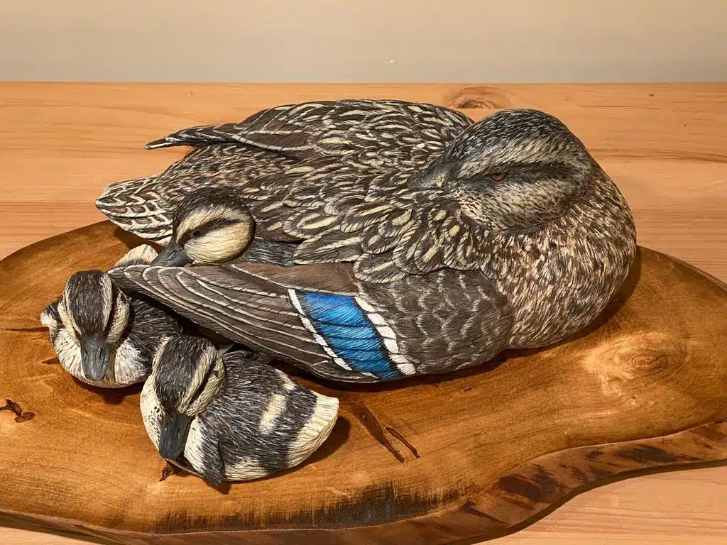 A carved wooden duck resting on a wooden base.