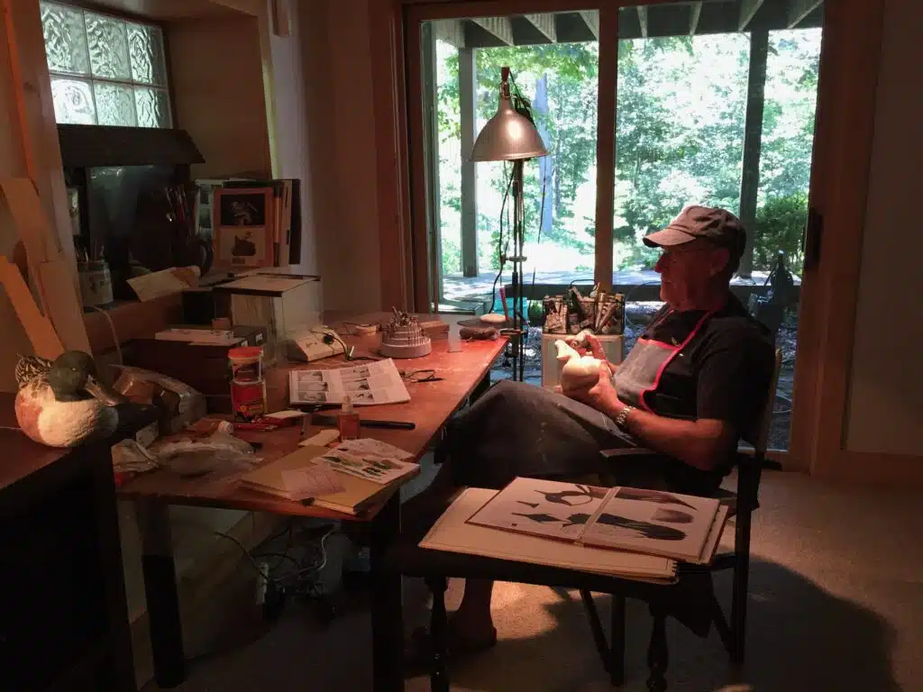 Man sitting and reading in a cozy room with large windows.